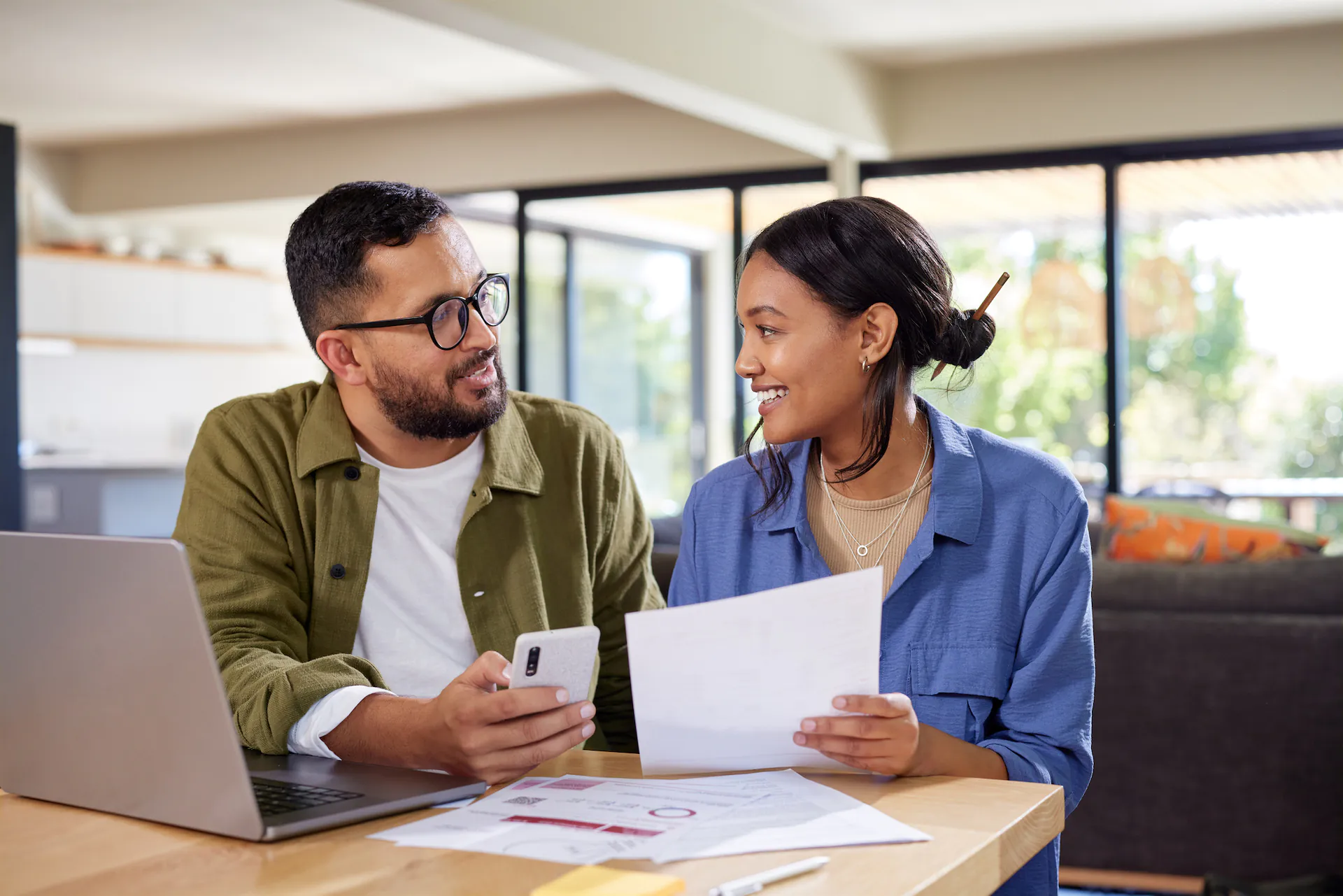 A happy couple discussing home finance while holding documents and working on laptop and mobile phone.